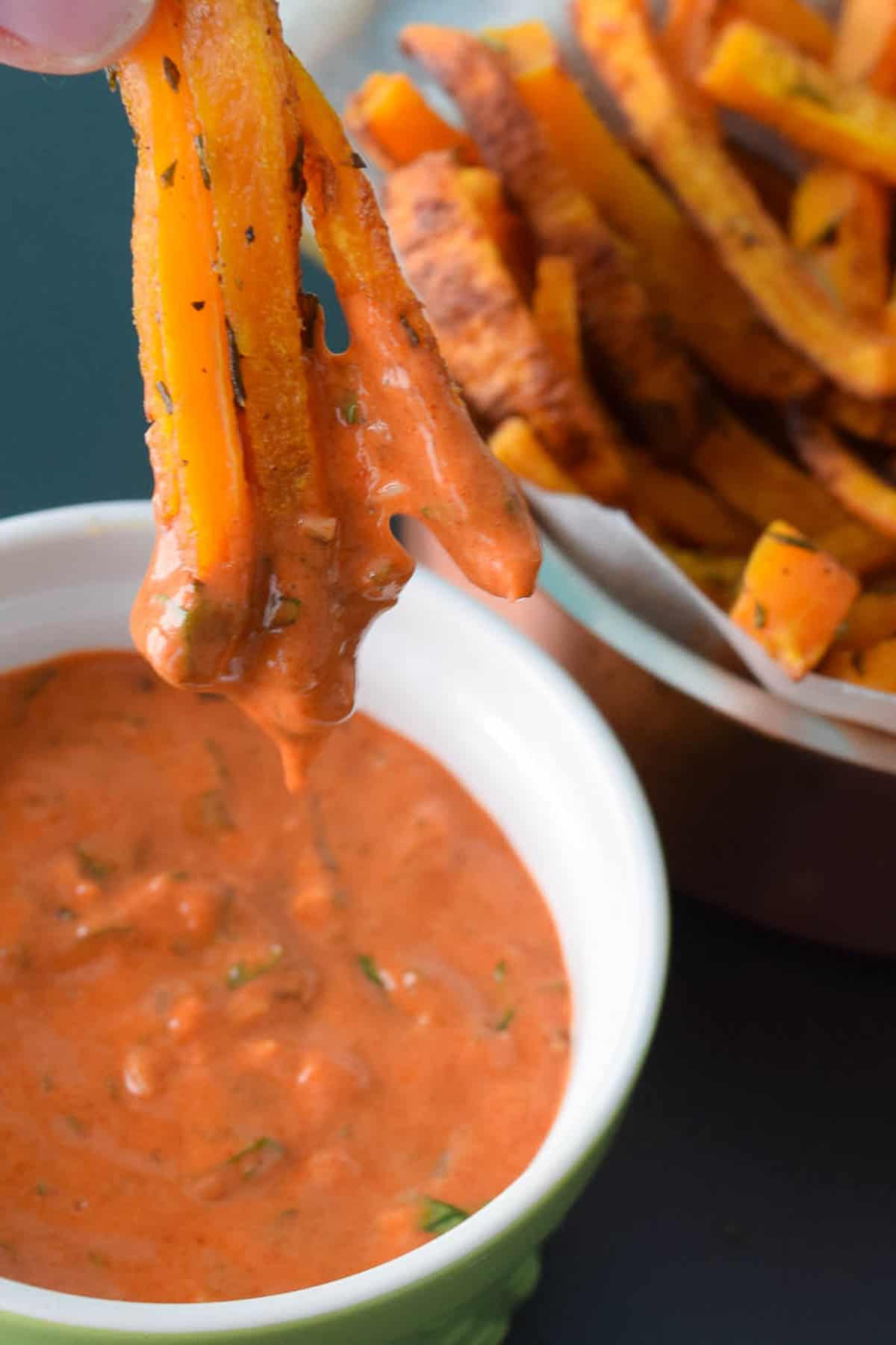 close up view of butternut squash fries being dipped into a red serving sauce