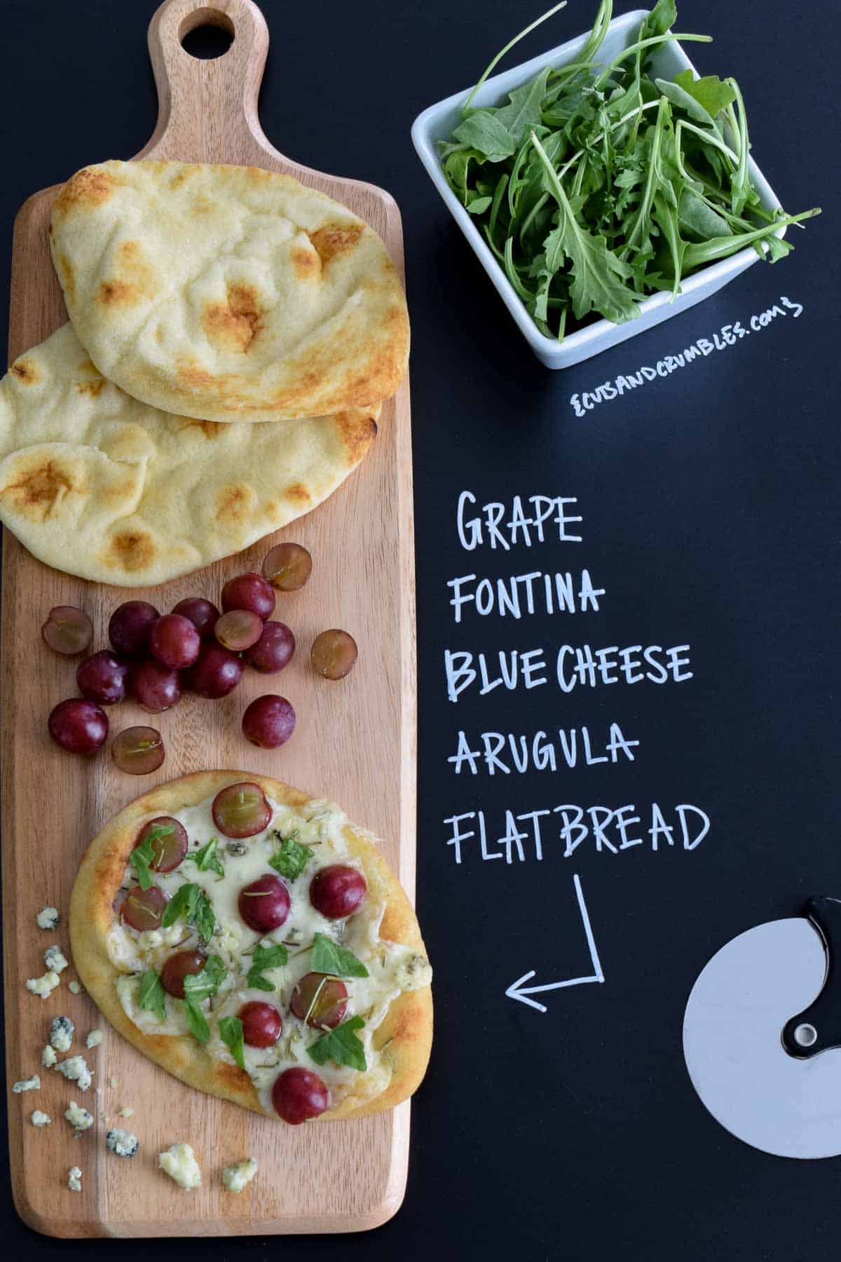 Grape Fontina Blue Cheese Arugula Flatbread on wooden serving board with title written in chalk